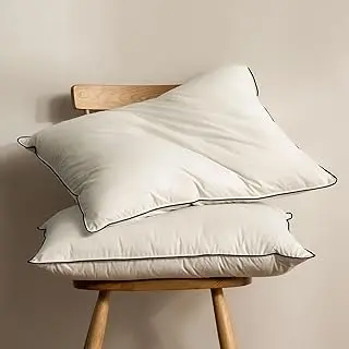 Dos almohadas blancas premium apiladas sobre silla de madera con fondo neutro cálido